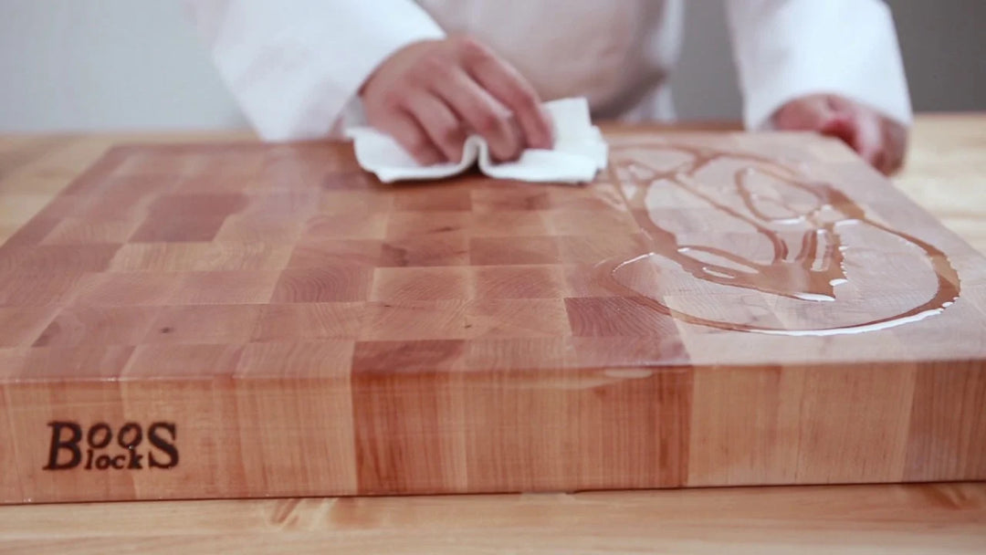 A wooden cutting board with hands in view coating it with oil to make the wood shiny