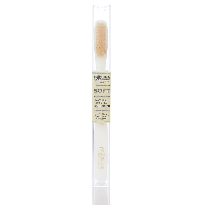 A white toothpaste with pale bristles by c o bigelow in a container with a label reading "soft natural bristle toothbrush"
