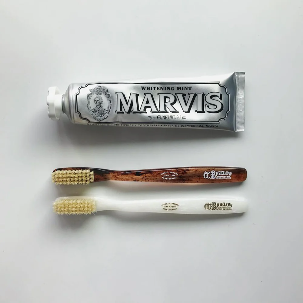 Marvis toothpaste tube and two Bigelow toothbrushes on a light gray background