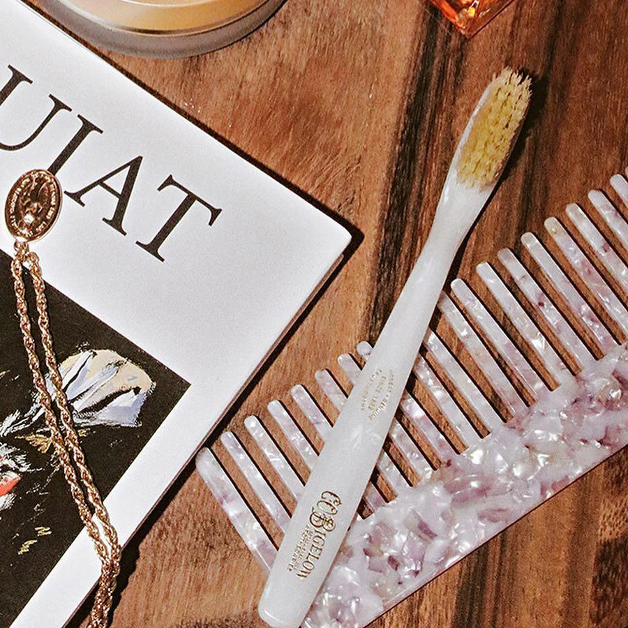 White toothbrush and comb on a wooden surface with a magazine and crystal container.