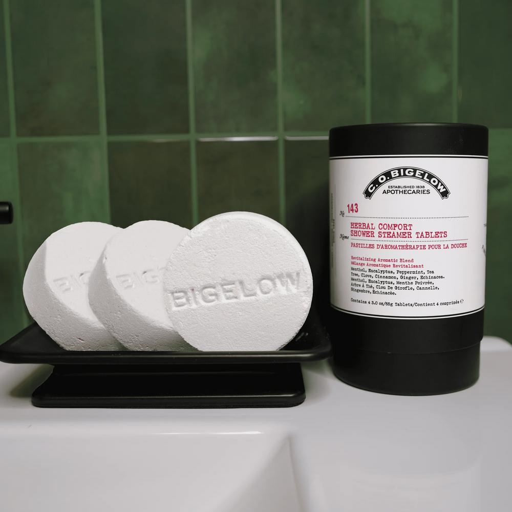 Bigelow Shower Steaming Tablets n a bathtub edge next to a black cylidrical container with a white label