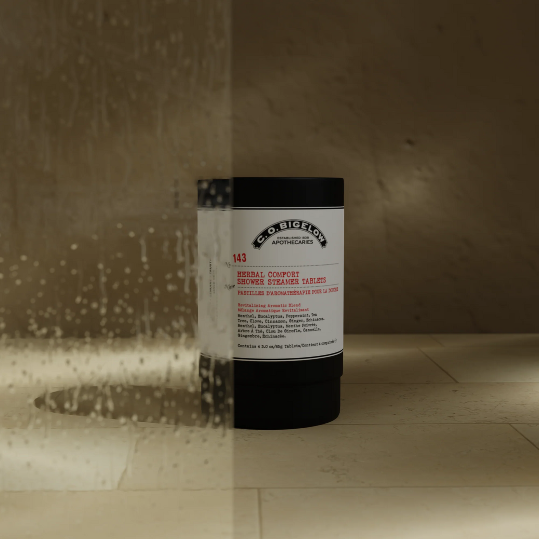 Container with a label reading "C O Bigelow Herbal Comfort Shower Steamer Tablets on a tiled shower floor 