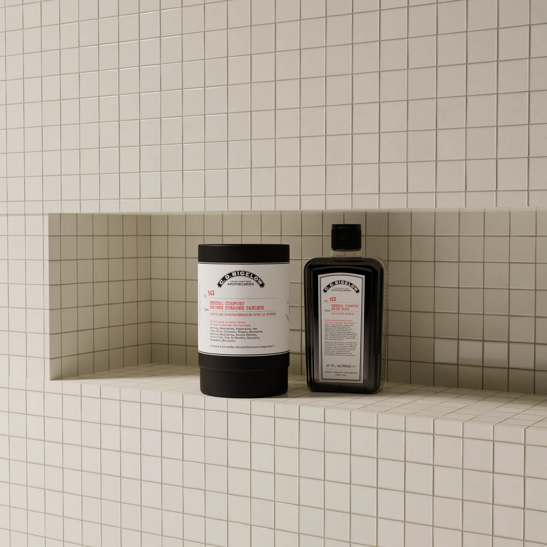 A container of Bigelow Shower Steamer Tablets on a tiled shelf against a tiled shower wall.