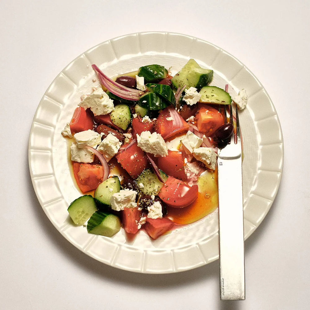 Plated salad with tomatoes, cucumbers, and feta cheese on a white plate with a weird fork.