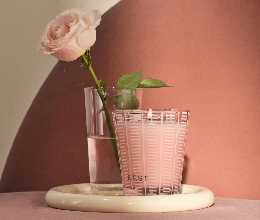 Nest Himalayan Salt and rosewater classic candle in front of a glass of water with a pink rose in it