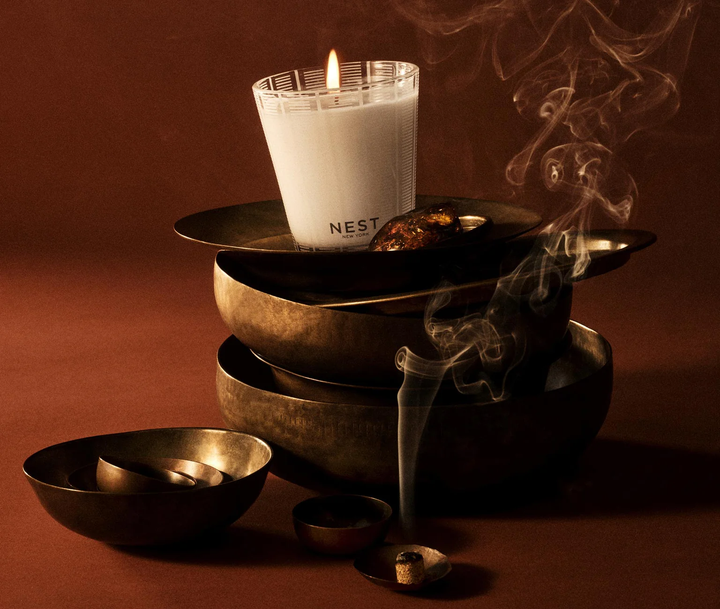 Nest Moroccan amber candle itting on a stack of bowls next to burning cone incence