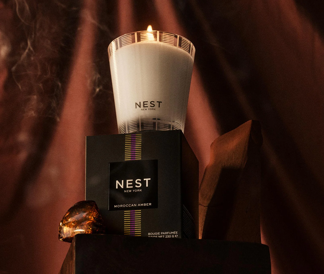NEST moroccan amber candle and packaging with a warm glow on a dark background