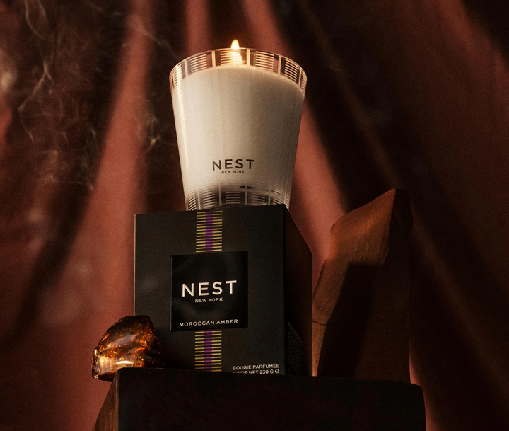 NEST moroccan amber candle and packaging with a warm glow on a dark background