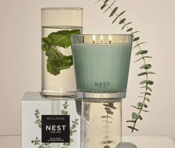 Green Wild Mint and Eucalyptus candle with 'NEST' branding next to a glass of water with mint leaves 