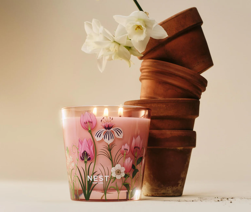 A decorative HImalayan Salt and rosewater Grande candle by nest sitting next to a stack of pots with daffodils