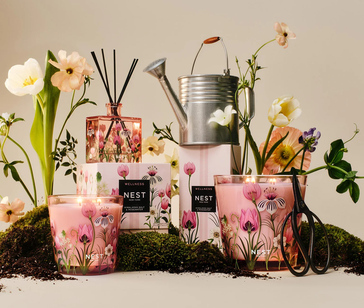 A decorative spread of Nest Himalayan Salt and Rosewater three wick and grande candle and reed diffuser with moss, tulips,  gardening shears, and a watering can 