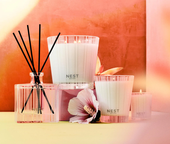 NEST three wick, classic, and votice candles and a reed diffuser witha rose of sharon flower on a soft pink background