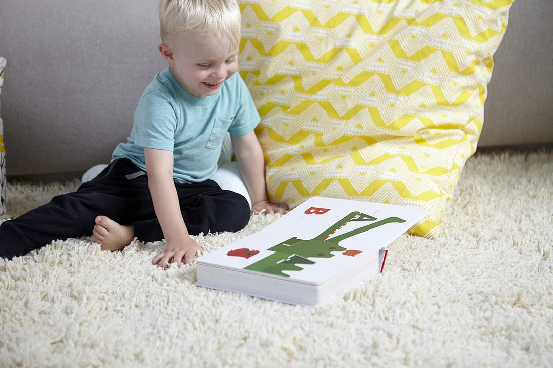 Child sitting on a white carpet with a colorful book in front of them, against a yellow and white patterned curtain.
