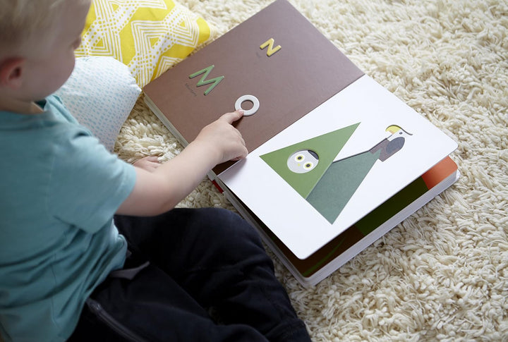 Child reading a book with letters and shapes on a carpeted floor