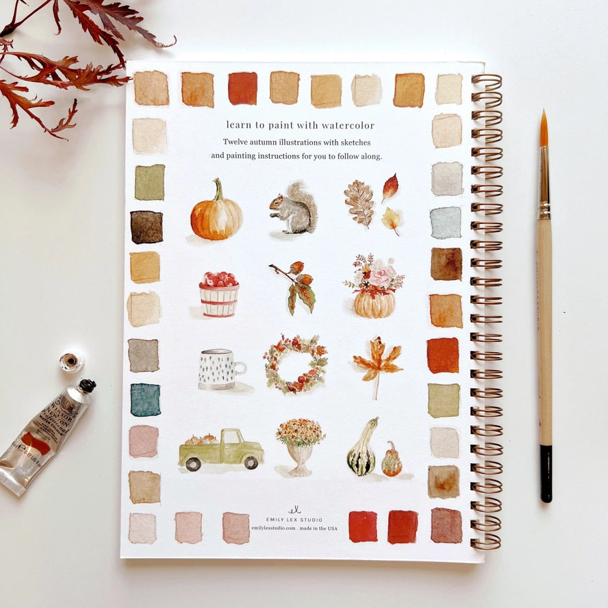 Artbook with watercolor illustrations of autumn elements next to a paintbrush