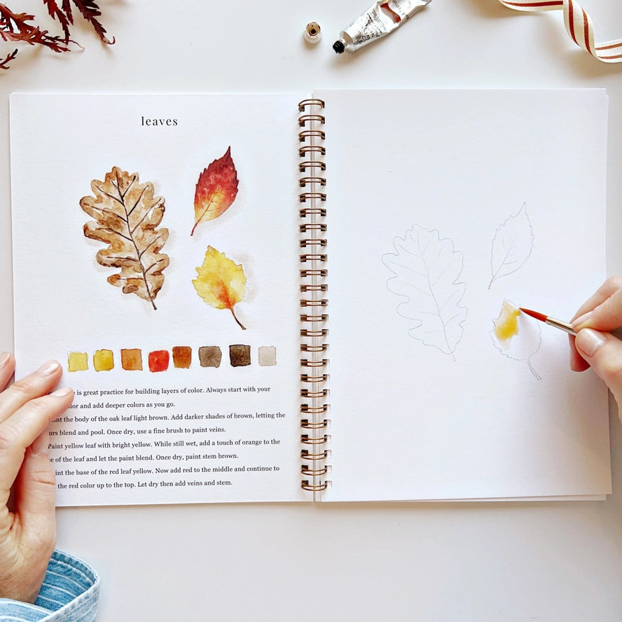 Open book with leaf illustrations and color swatches, being painted with a brush.