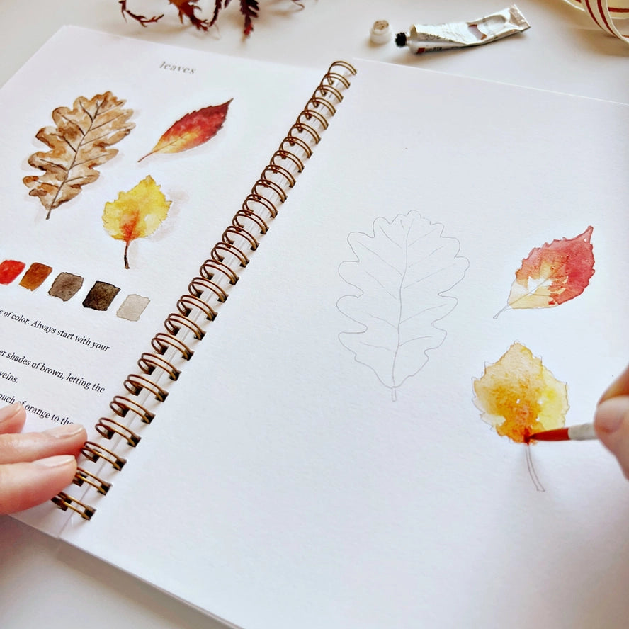 Person painting autumn leaves in a sketchbook with watercolors