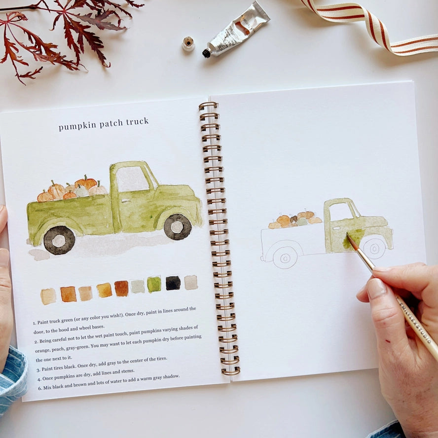 Open book with a green truck illustration, paintbrush, and color swatches on a white surface.