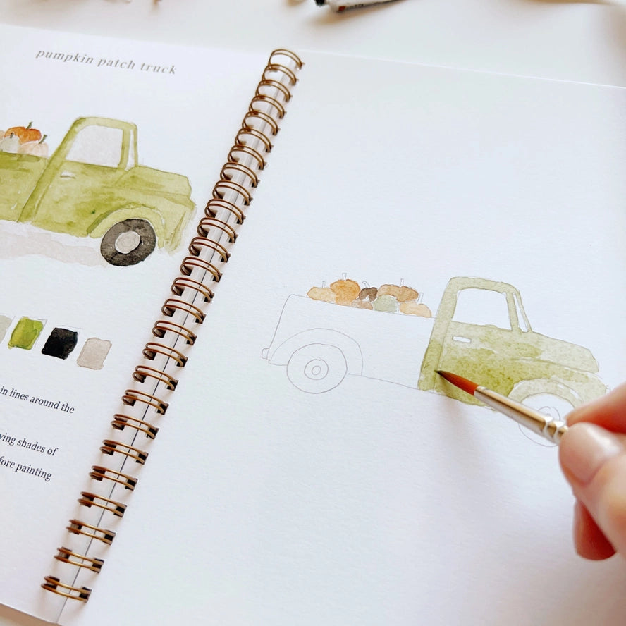 Person painting a watercolor truck on a spiral-bound notebook with a brush.