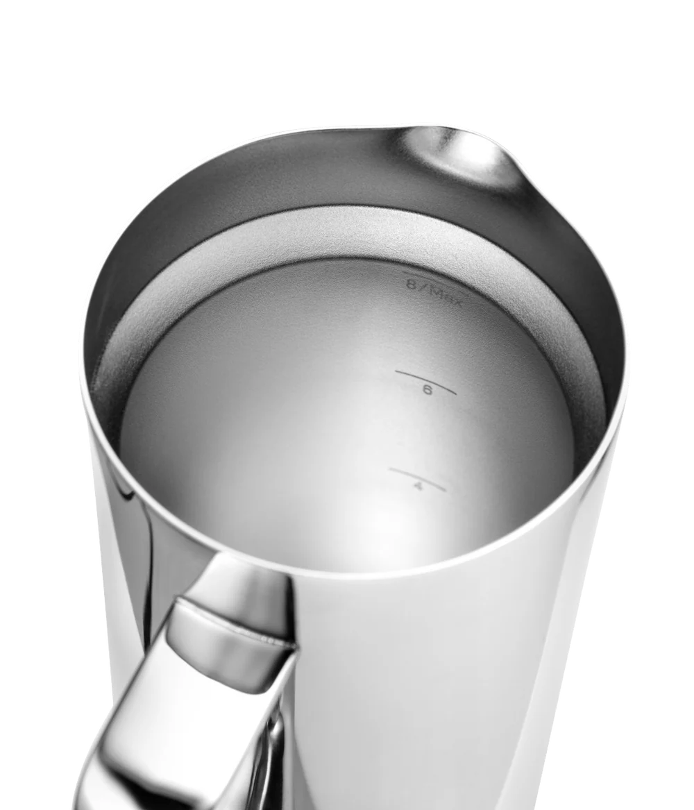 Close-up of a stainless steel milk pitcher with a pouring spout and handle, showing measurement markings inside on a white background.