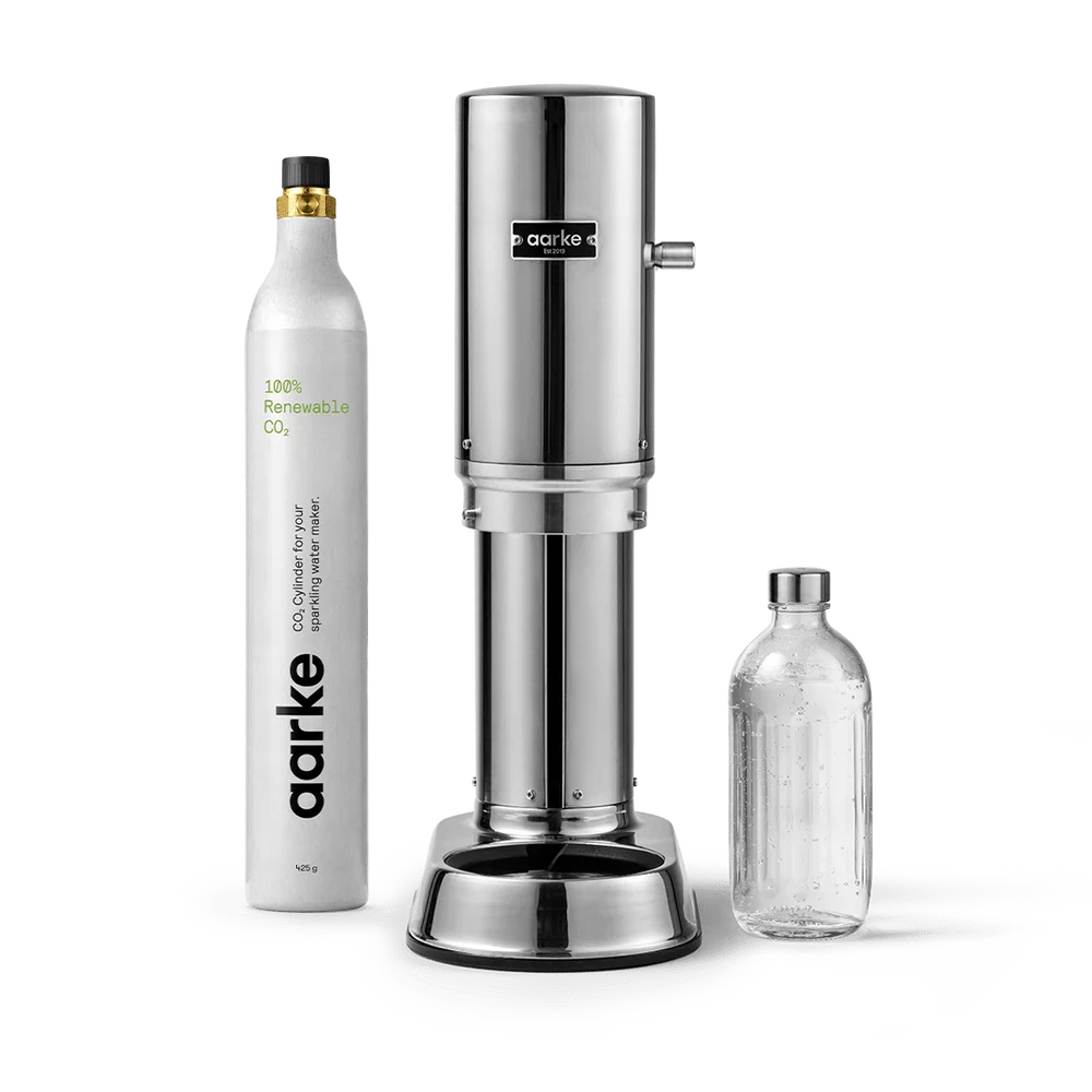 Aarke CO2 beverage maker set featuring a polished stainless steel carbonator machine, a white refillable CO2 cylinder, and a clear glass bottle on a white background.