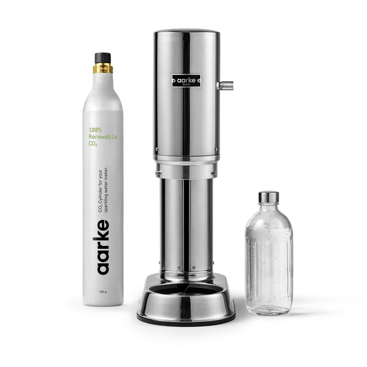 Aarke CO2 beverage maker set featuring a polished stainless steel carbonator machine, a white refillable CO2 cylinder, and a clear glass bottle on a white background.