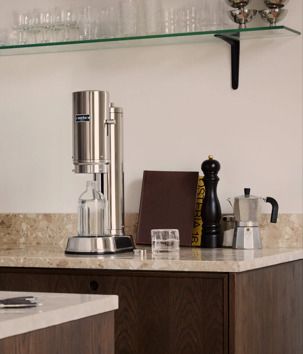 Stainless steel coffee maker on a kitchen counter with a glass shelf in the background.