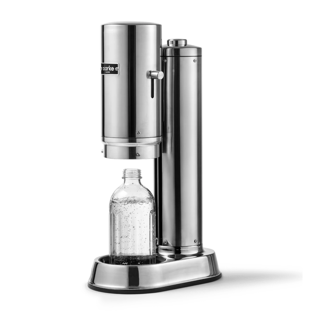 A stainless steel soda maker with a clear plastic bottle placed under the dispensing head, shown on a clean white background.