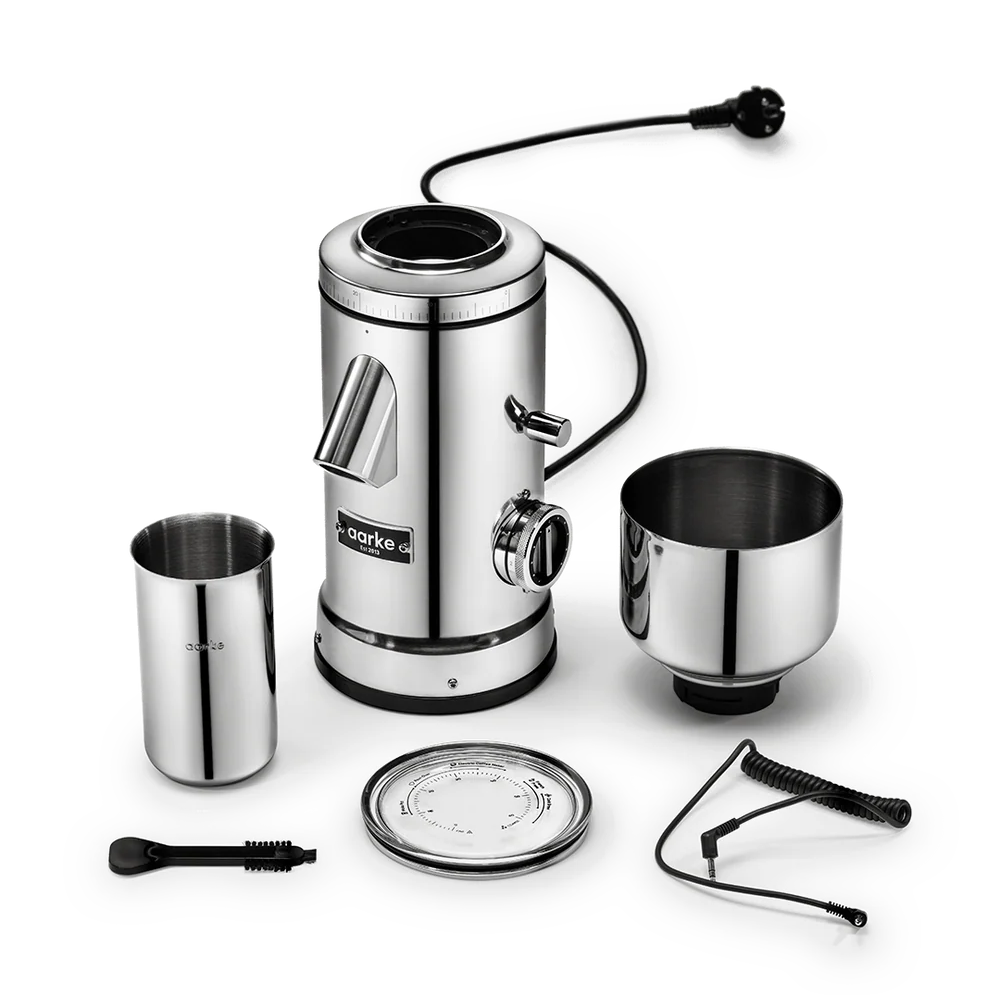 A stainless steel electric coffee grinder set with its accessories, including a metal bean hopper, a metal bowl, a lid, a cleaning brush, and a coiled cord, arranged on a clean white background.