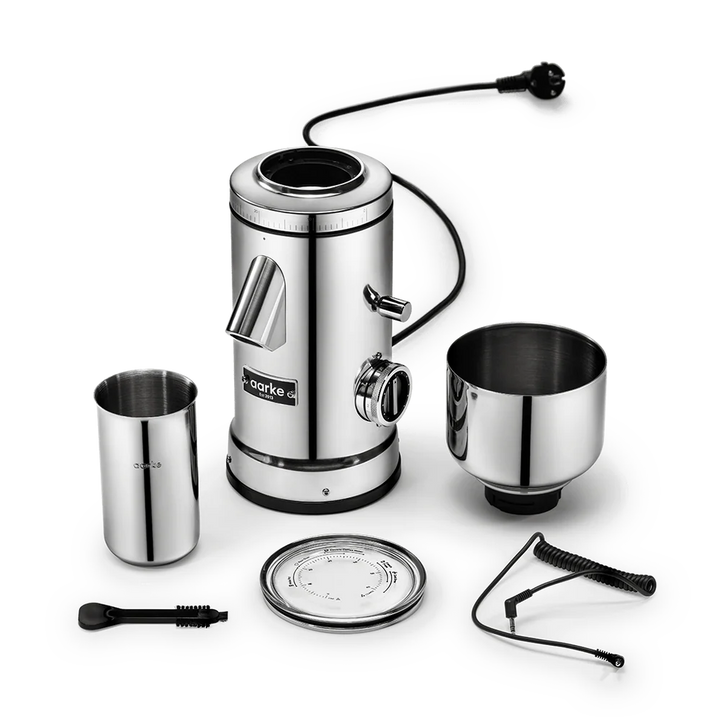 A stainless steel electric coffee grinder set with its accessories, including a metal bean hopper, a metal bowl, a lid, a cleaning brush, and a coiled cord, arranged on a clean white background.