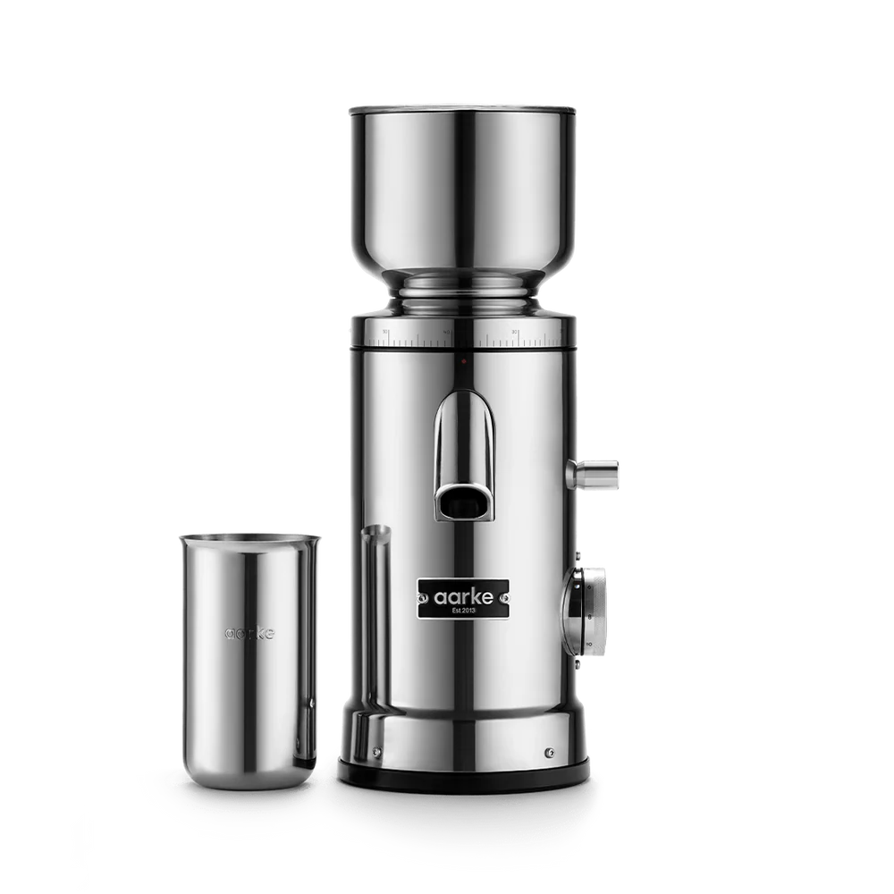 A stainless steel manual coffee grinder with a separate metal cup, shown on a clean white background. The brand name 'aarke' is clearly visible on the front of the grinder.