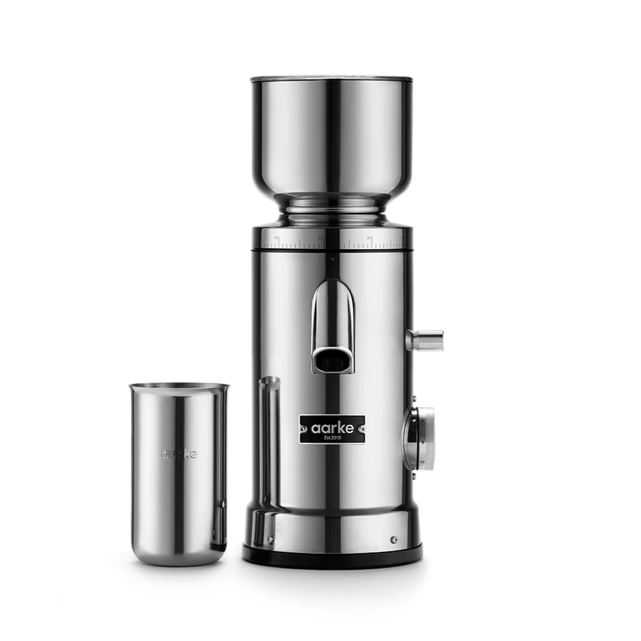 A stainless steel manual coffee grinder with a separate metal cup, shown on a clean white background. The brand name 'aarke' is clearly visible on the front of the grinder.