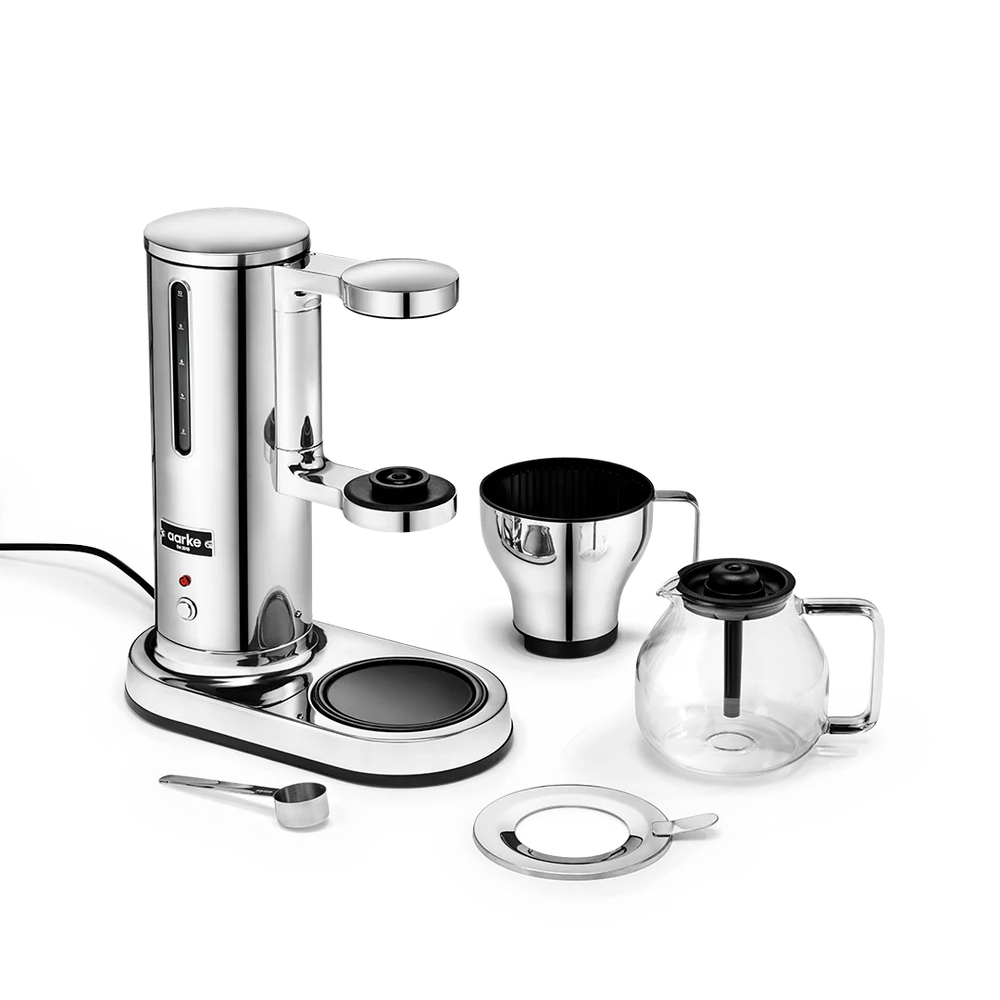 A stainless steel espresso machine set with a glass carafe, metal filter basket, measuring scoop, and lid, arranged on a clean white background.