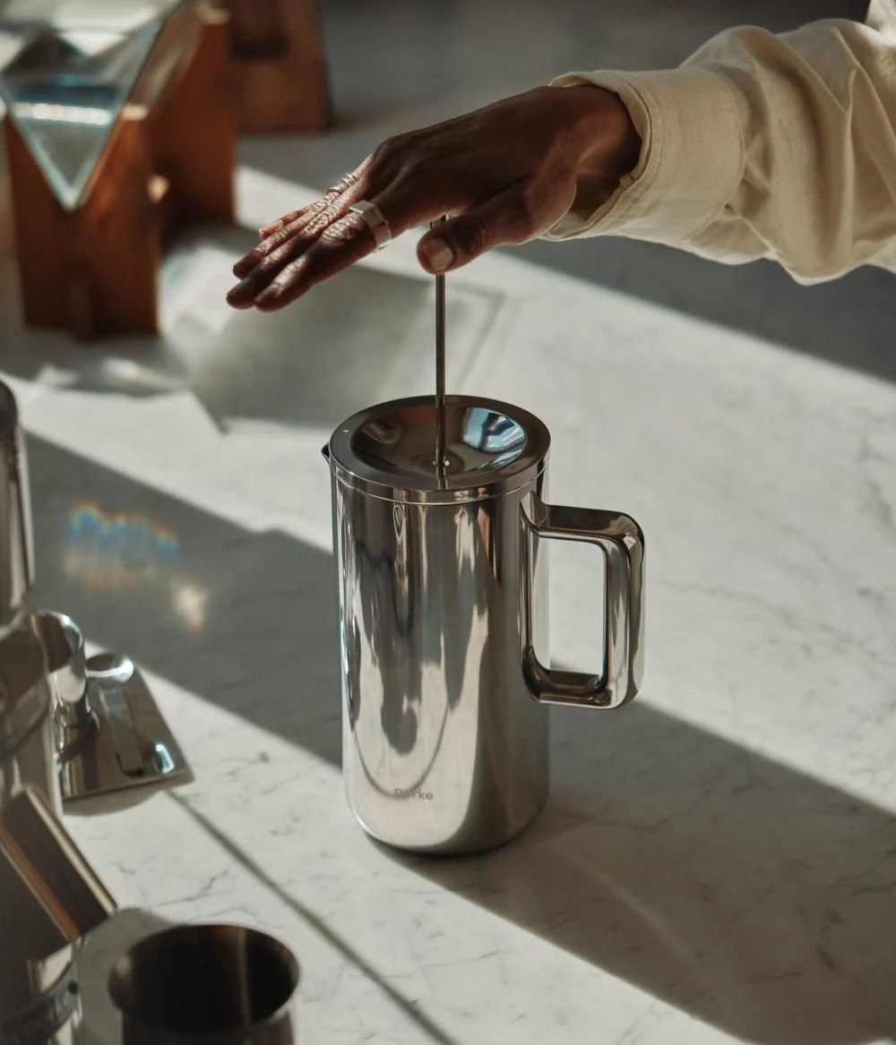 Person using a stainless steel French press on a marble surface