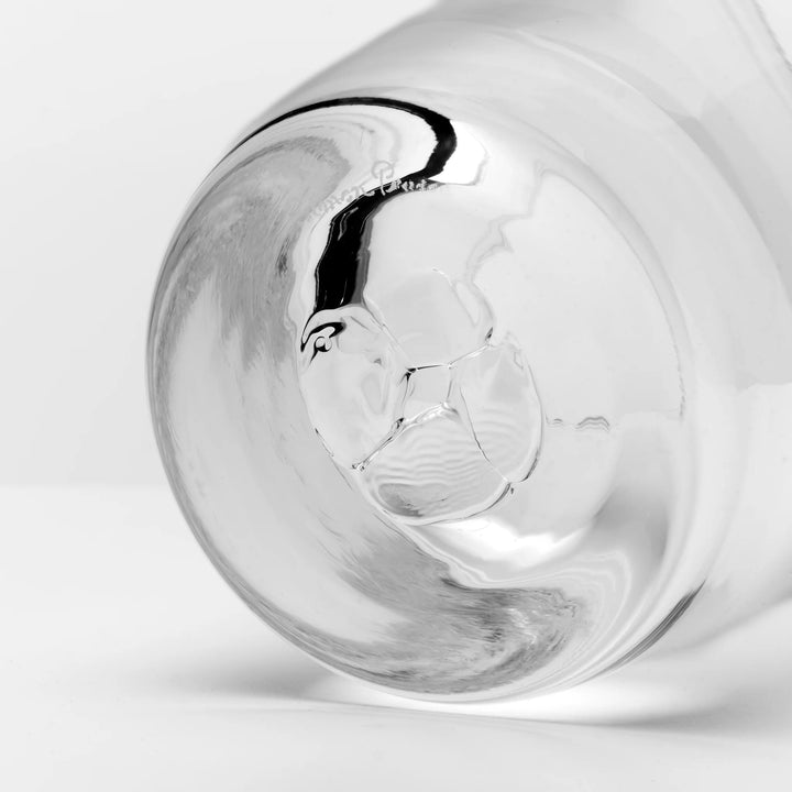 A close-up studio shot of a clear glass tumbler or cup base with a glossy reflective surface on a light gray background.