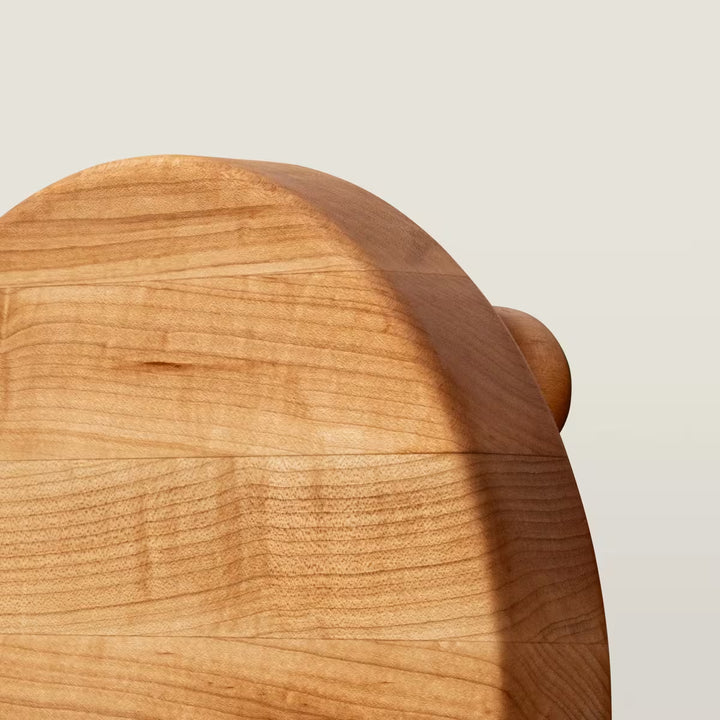 Close-up of a light natural wood product, showing the grain and rounded curved edge against a plain light gray background.