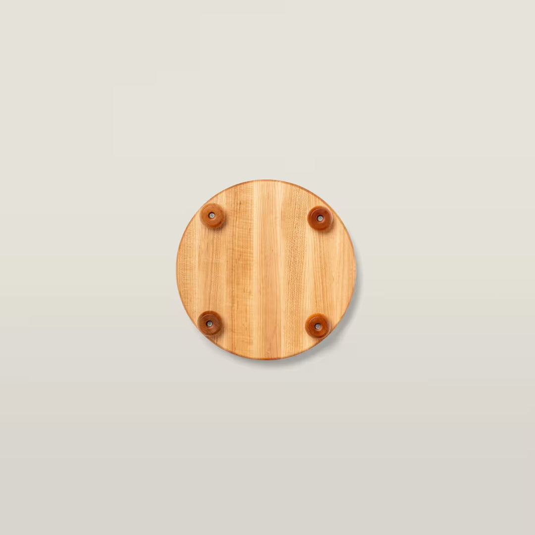 A round light brown wooden board with four small brown rubber feet, shown from a top-down view on a light beige background.