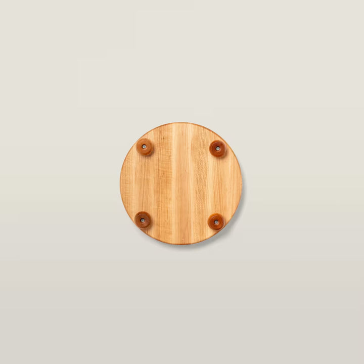 A round light brown wooden board with four small brown rubber feet, shown from a top-down view on a light beige background.