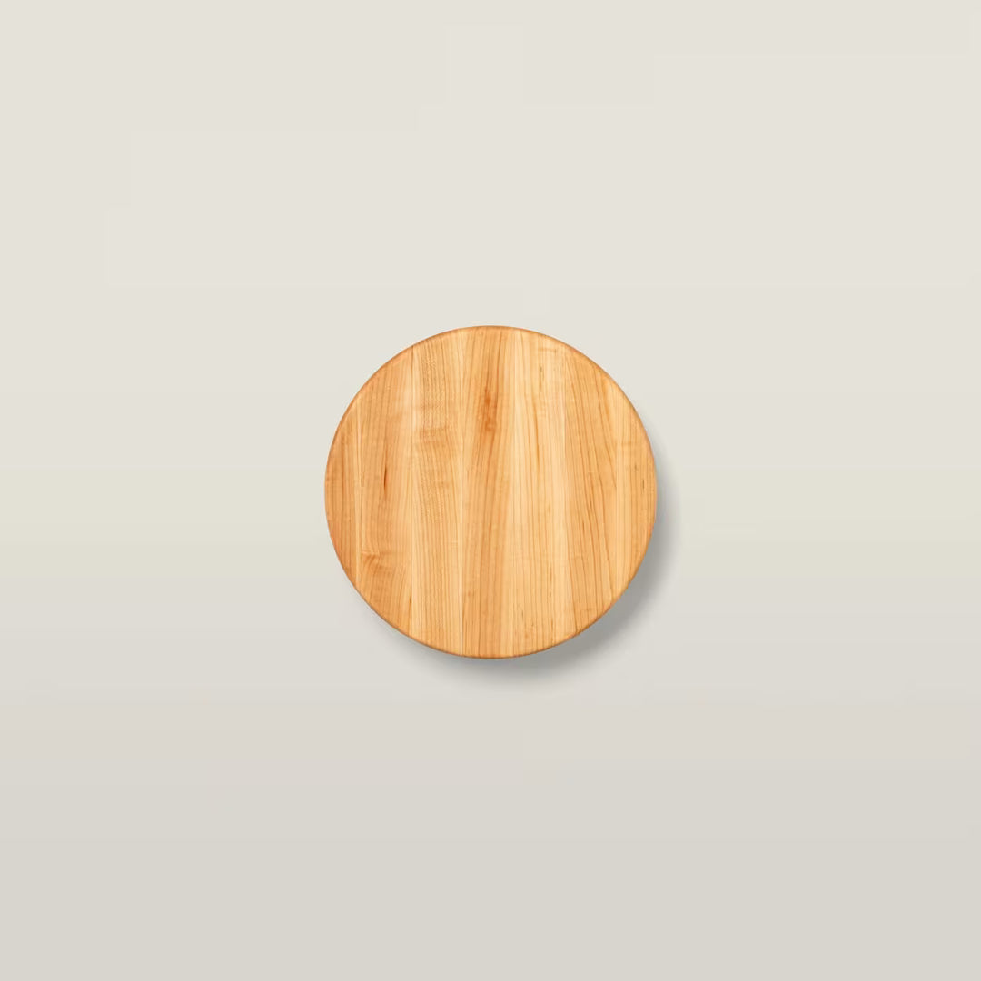 A round wooden board or coaster with a light natural wood grain finish, centered on a light gray background.