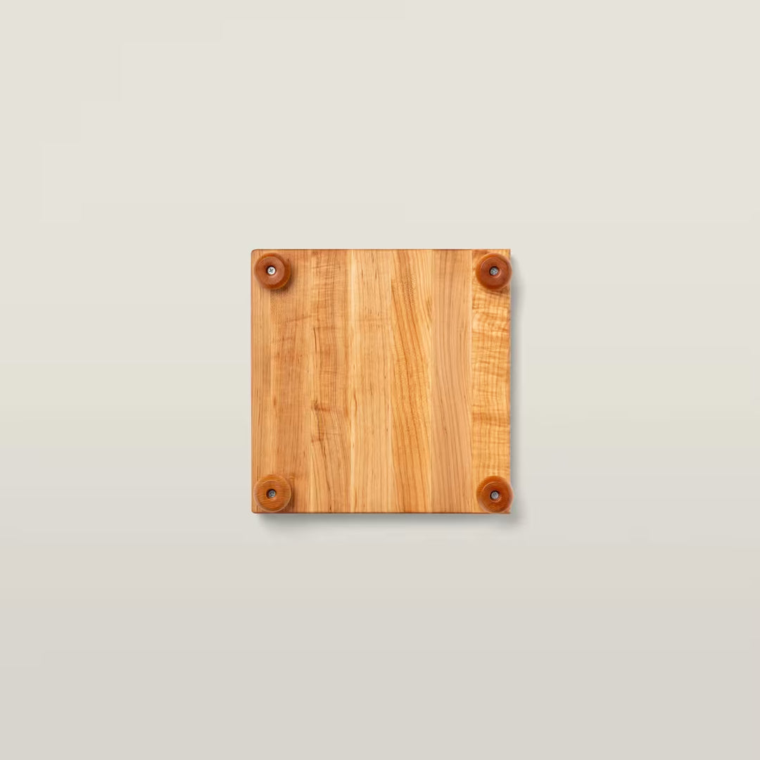 A square wooden board with a warm honey-toned wood grain finish and four small round brown feet or wheels attached at the corners, shown from above on a light beige background.
