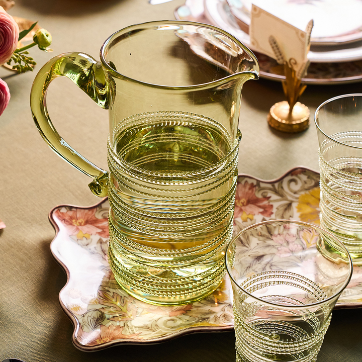 Clear glass pitcher and glasses on a decorative table setting with floral elements.