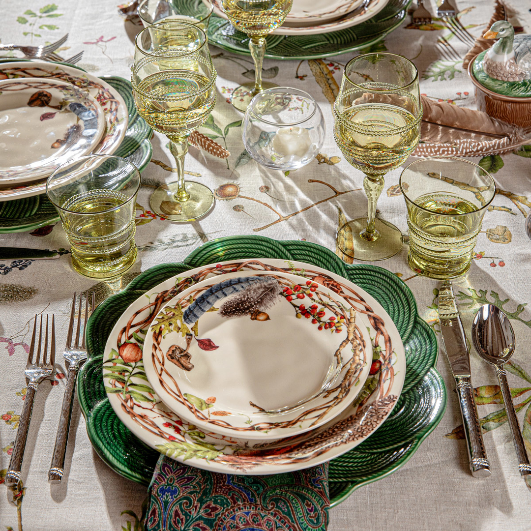 Dining table setting with patterned plates, glasses, and cutlery on a decorative tablecloth.