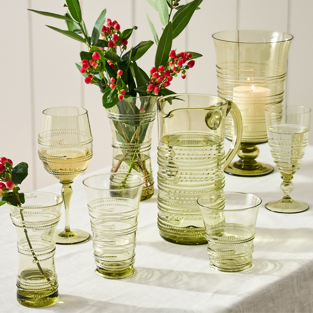 Set of green glassware including cups, a pitcher, and a vase with flowers on a white surface.