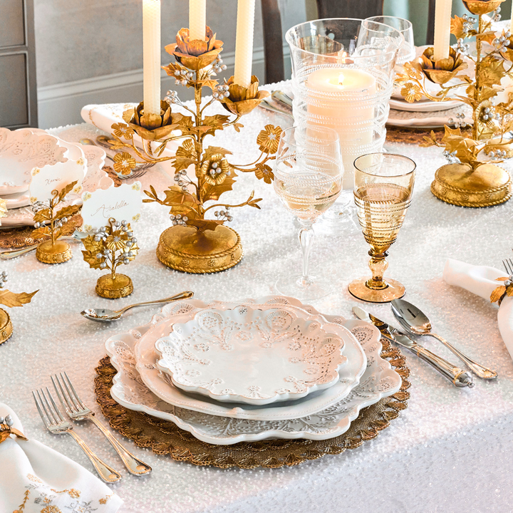 Elegant table setting with gold candle holders, glassware, and decorative plates on a white tablecloth.