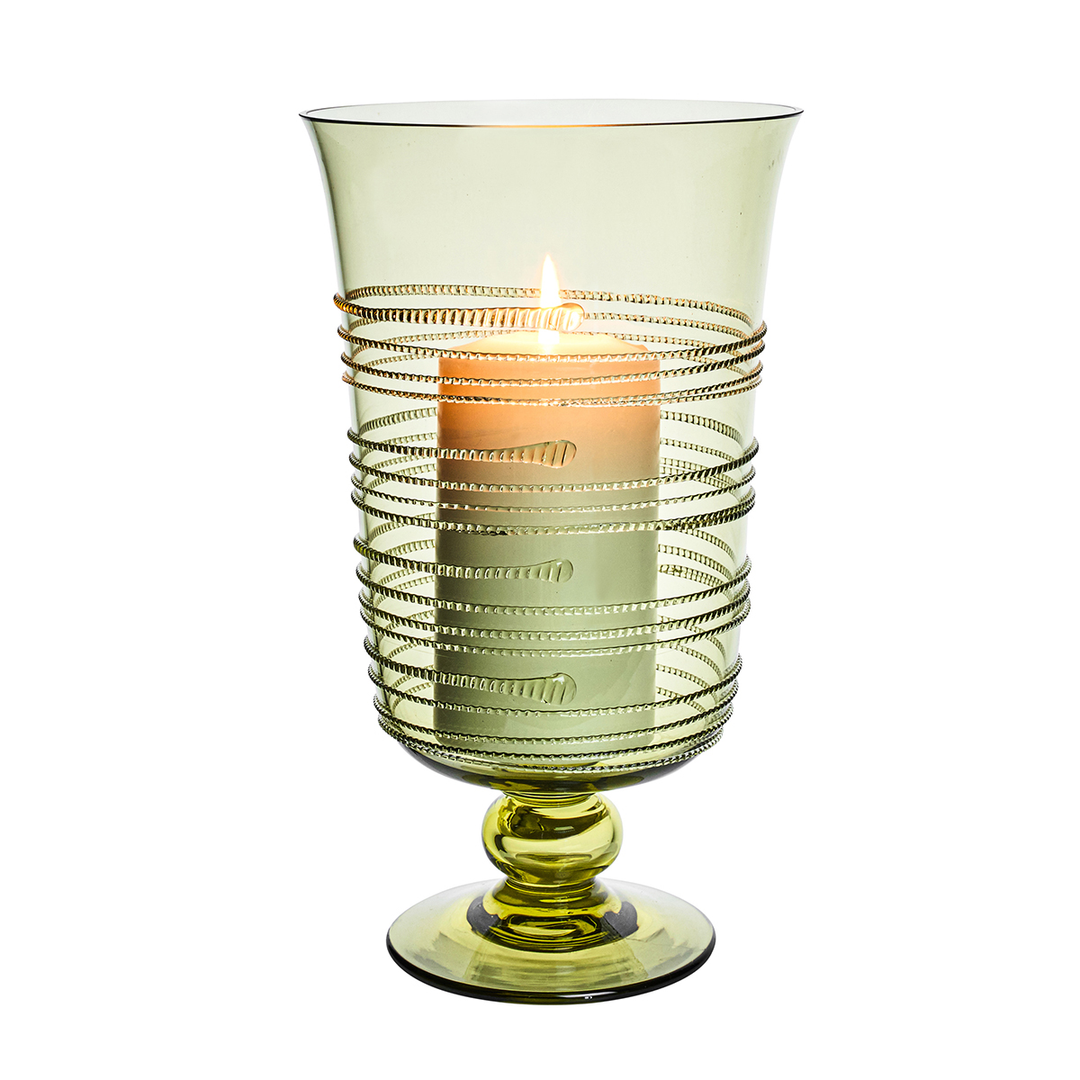 Green glass candle holder with a lit candle inside on a white background