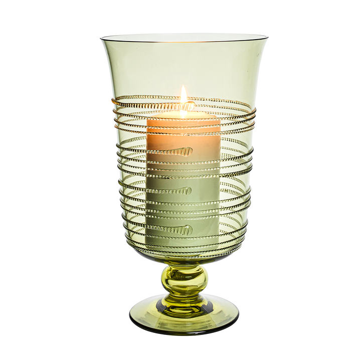 Green glass candle holder with a lit candle inside on a white background