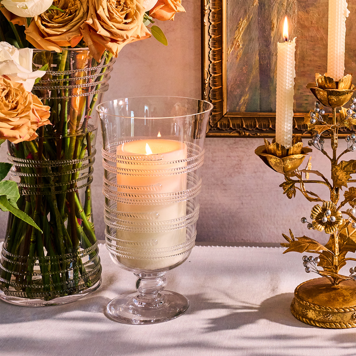 Decorative setup with a glass candle holder, flowers, and a gold candelabra on a table.