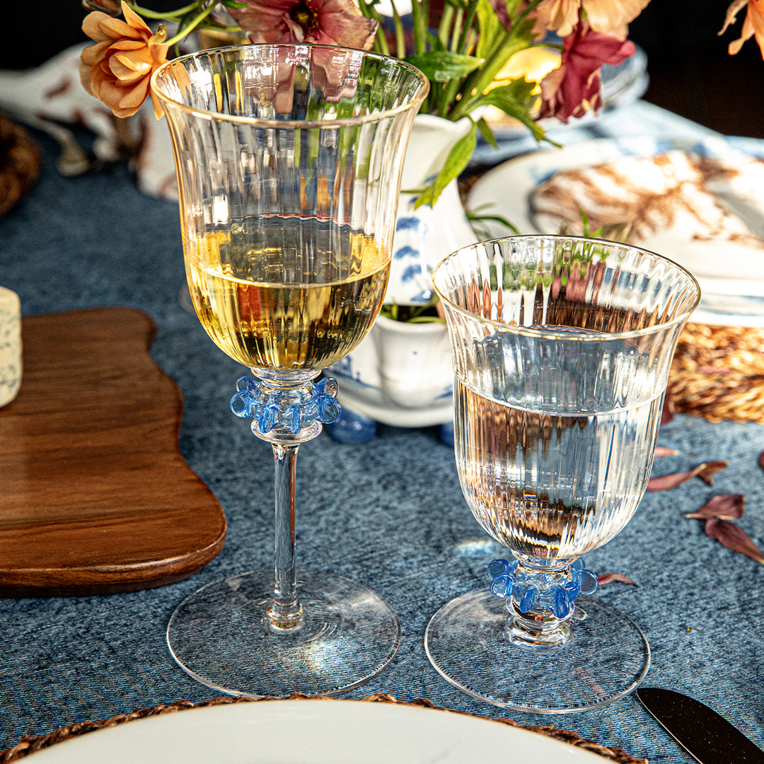 Two glasses, one with white wine and the other with water, on a table setting with flowers and plates.