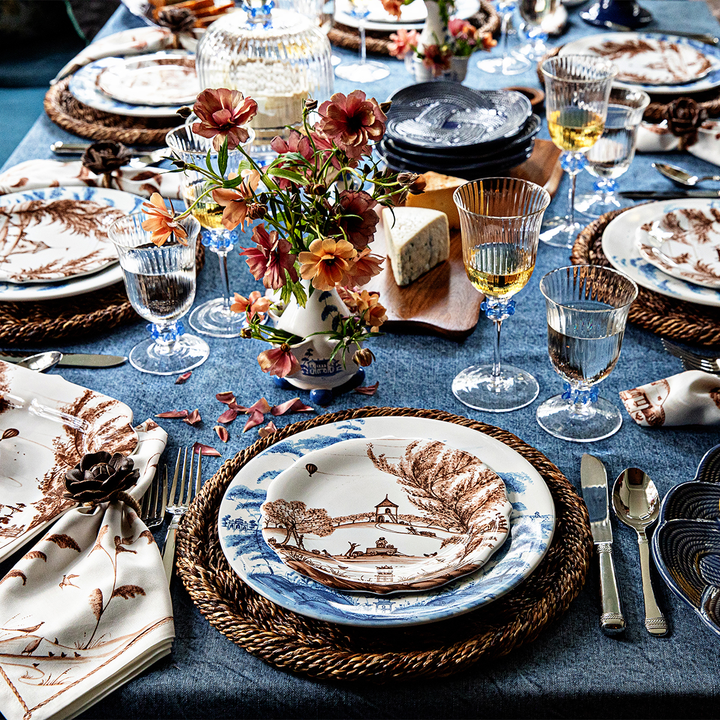 A set table with delft and sepia design plates on wicker chargers and a denim tablecloth