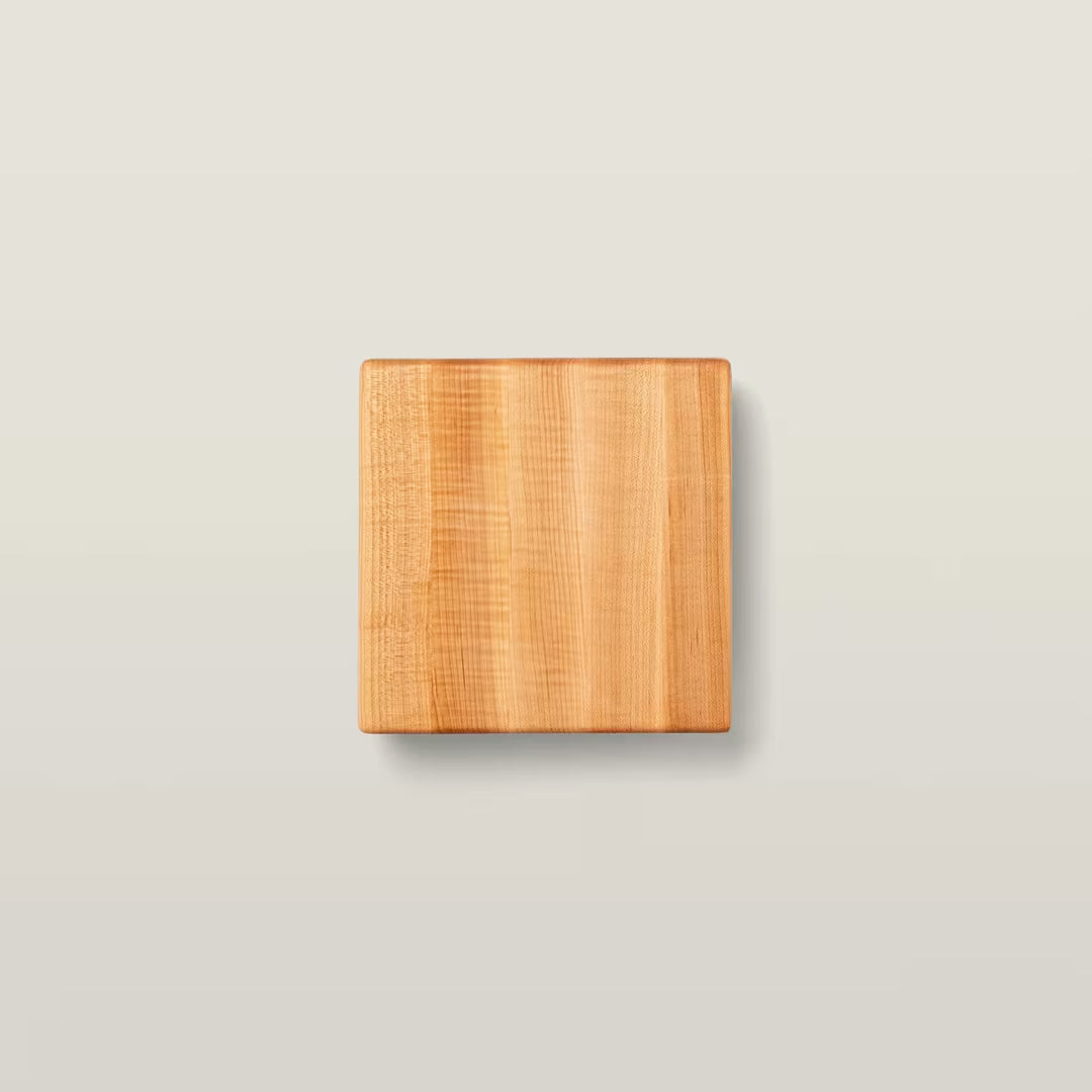 A square wooden cutting board with a natural light brown grain, centered on a light beige background.